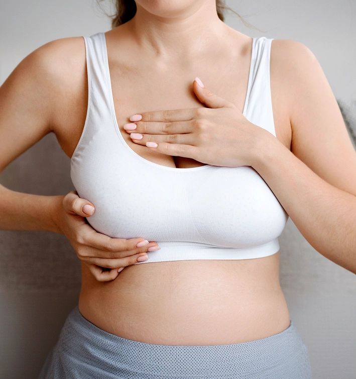 A woman wearing a white sports bra placing her hands on her breast during a breast self-examination for early detection.