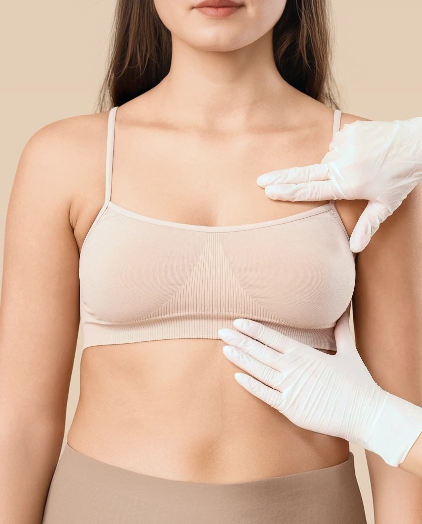 A medical professional in white surgical gloves examining a patient wearing a beige crop top during a clinical breast assessment.