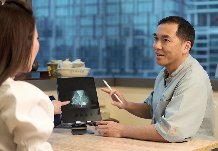 Dr. Evan Woo explaining mammogram scan results on a tablet to a female patient during a consultation.