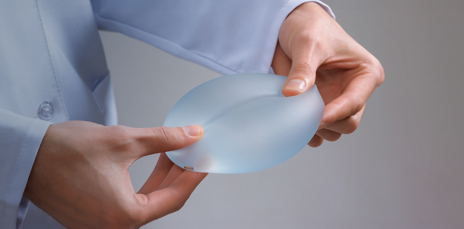Doctor in a lab coat holding and demonstrating a flexible silicone breast implant