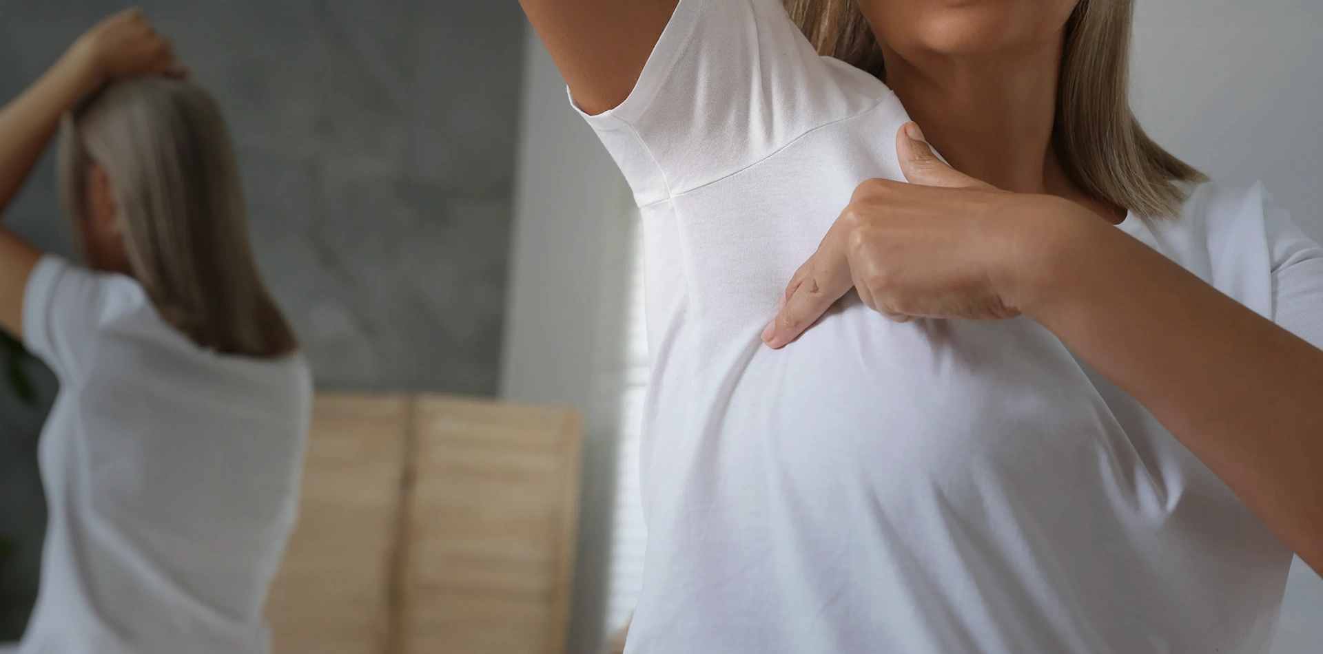 Woman in a white shirt performing a breast self-examination in front of a mirror