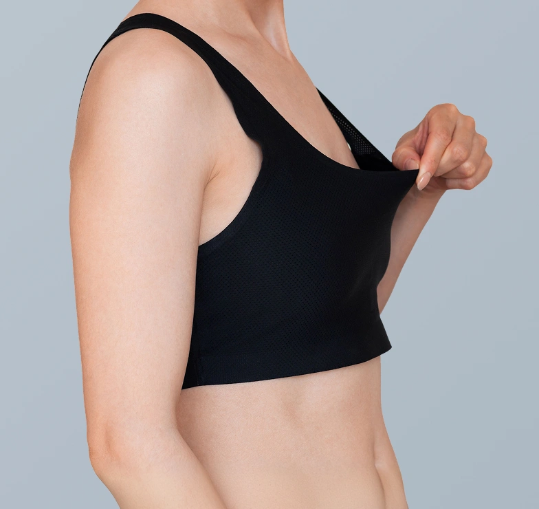 Side profile of a woman wearing a supportive black surgical crop top following breast surgery recovery.