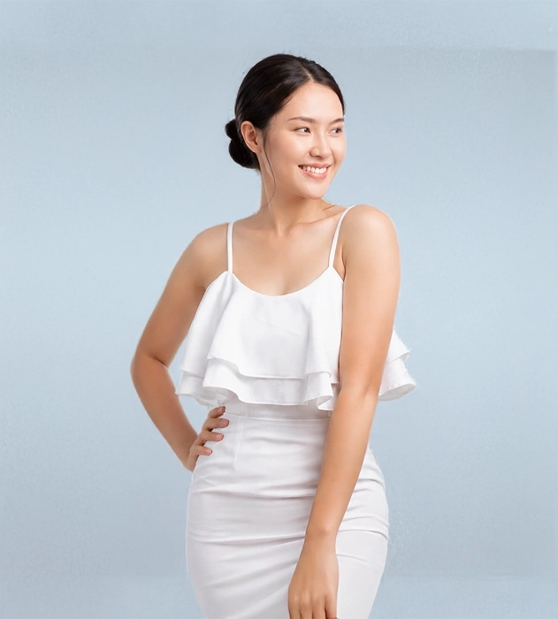 Smiling Asian woman with smooth skin wearing a white ruffled top against a light blue background.