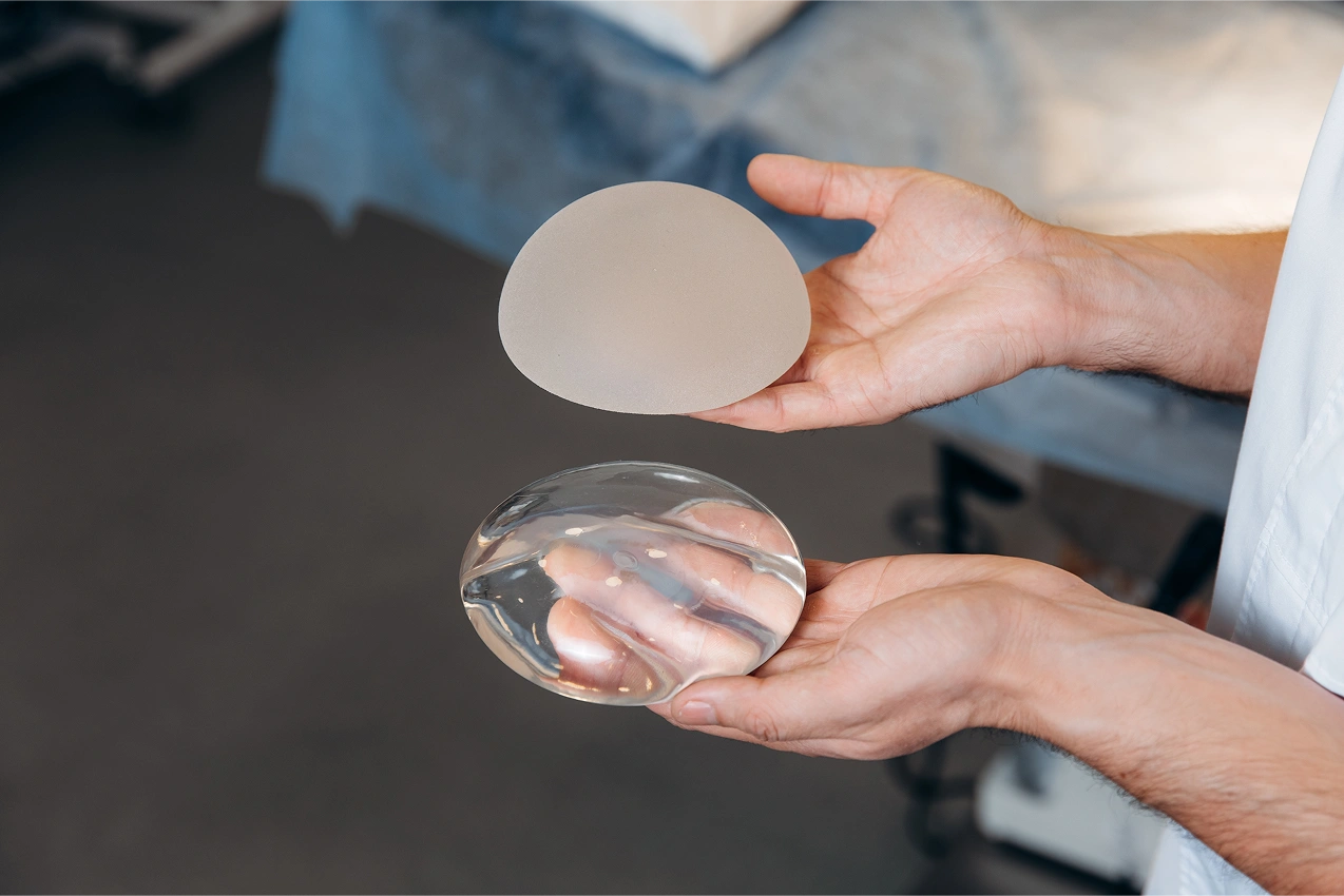 Surgeon holding a textured silicone breast implant and a clear smooth silicone breast implant for comparison.