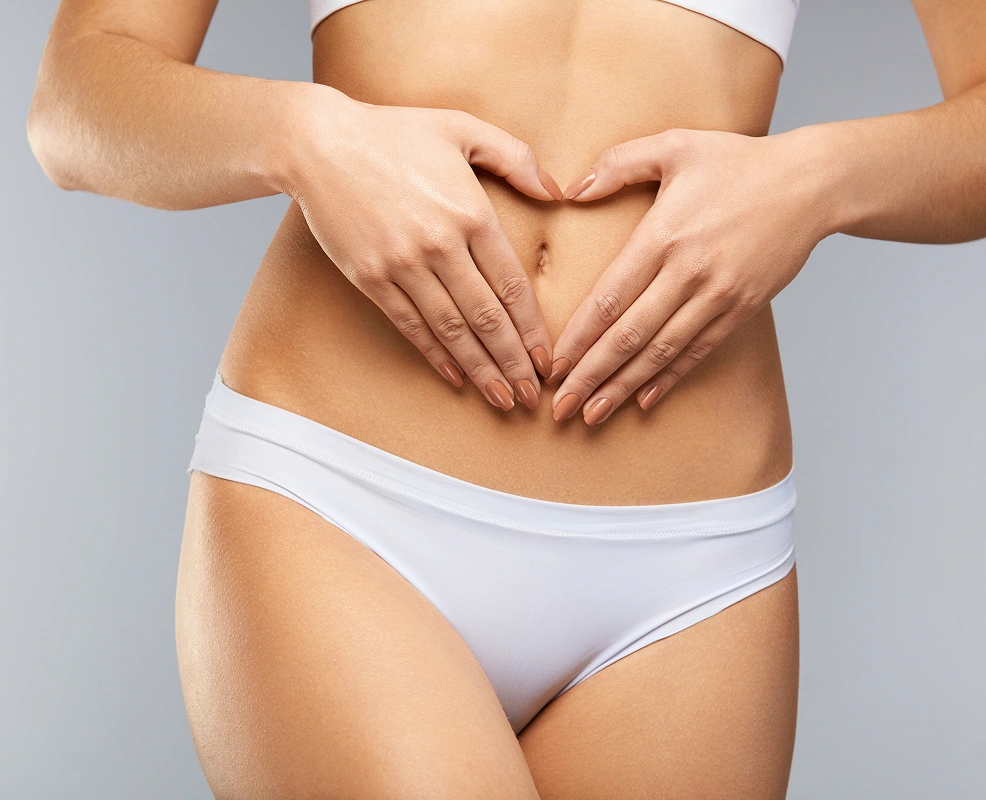 Close-up of a woman in white underwear forming a heart shape with her hands over her flat stomach.