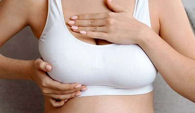 Close-up of a woman in a white sports bra performing a breast self-examination.