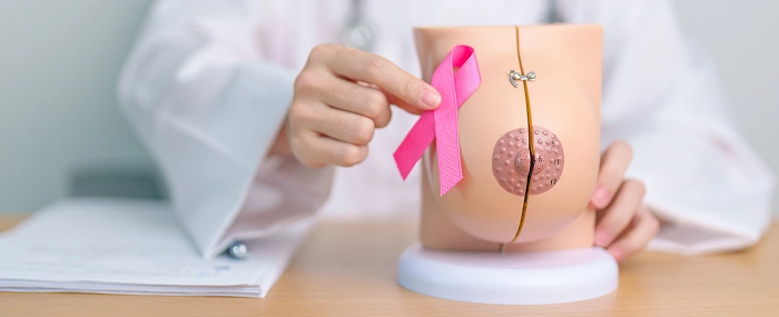 A doctor holding a pink ribbon next to an anatomical breast model during a breast cancer surgery consultation.